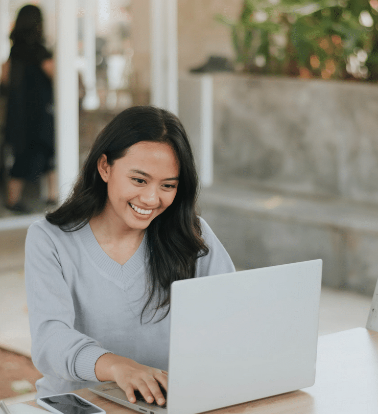 A smiling woman working on a laptop in a bright room, exploring the benefits of a WordPress Care Plan.