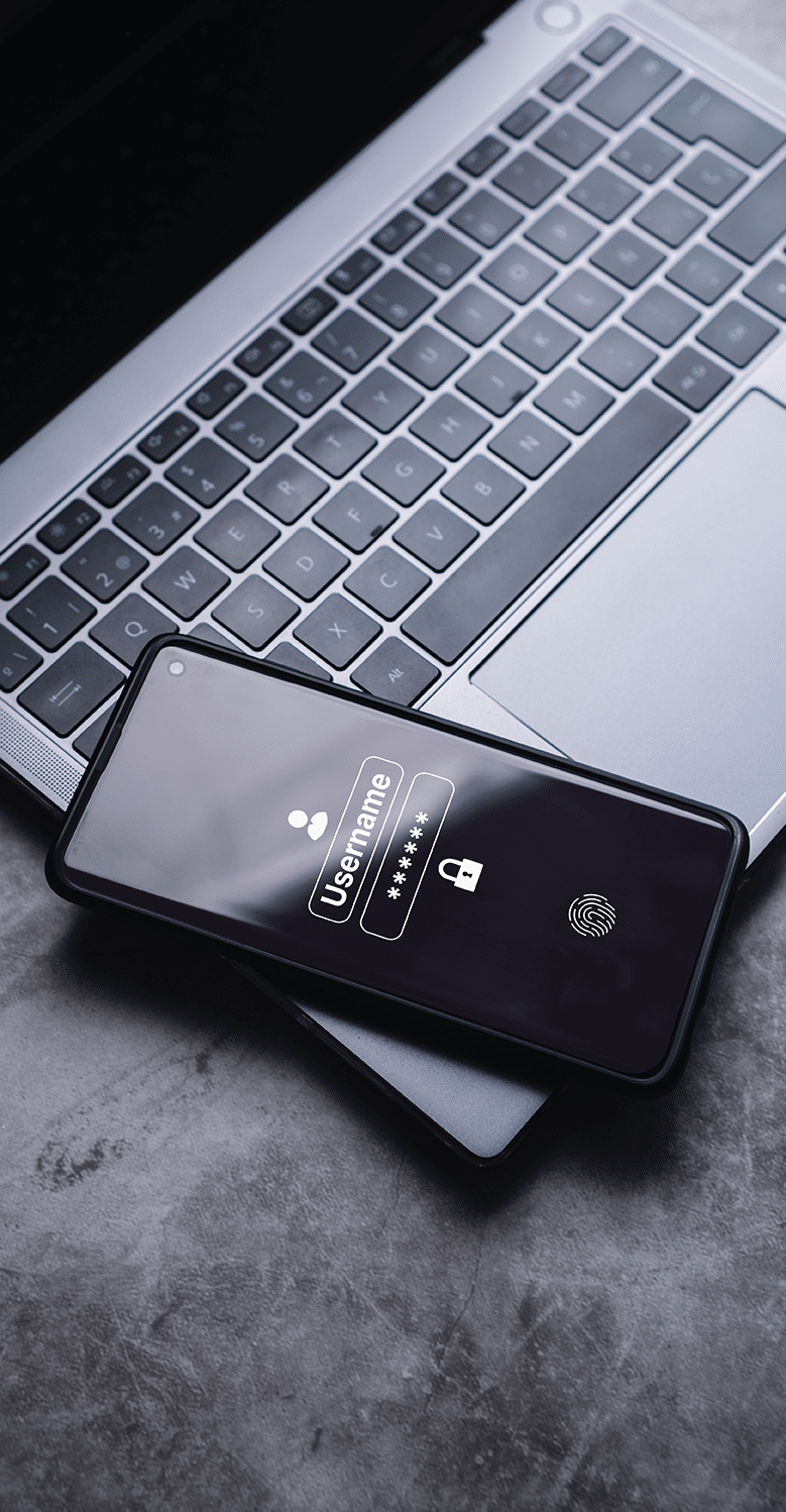 A smartphone displaying a login screen with username and password fields rests on a laptop keyboard. The phone screen also shows fingerprint authentication.