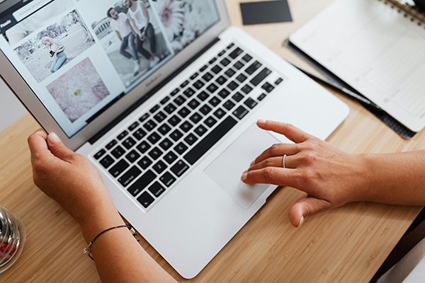 Implement Lazy Loading for Media and Embeds A person uses a laptop, viewing a webpage displaying several photos, with one hand on the keyboard and the other on the trackpad.