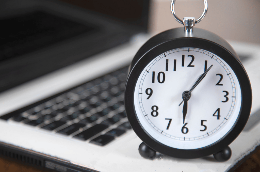 A black analog alarm clock showing 1:06 is placed on the keyboard of an open laptop.
