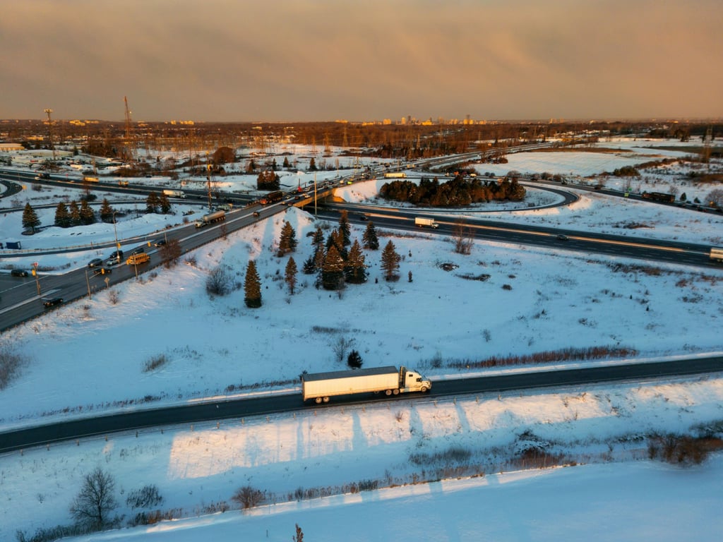 A semi-truck driving on a snowy highway at sunset