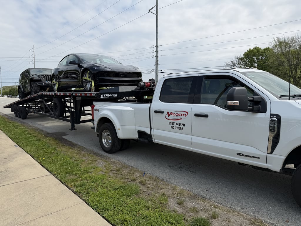 Velocity Logistics branded Ford F-350 dually towing a Stryker wedge carrier loaded with a Tesla and a Jeep Wrangler