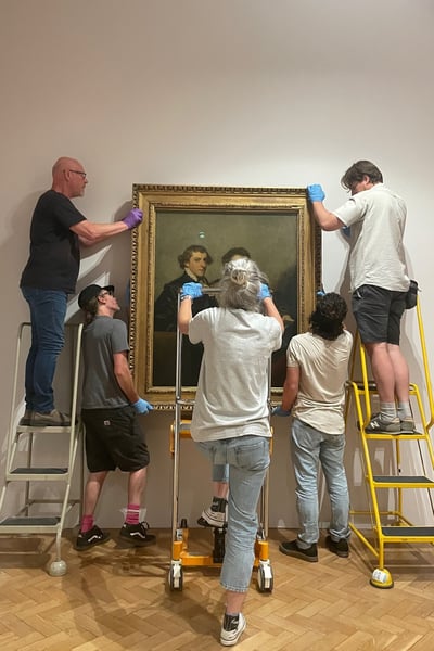 A group of people hang a heavy painting on a gallery wall
