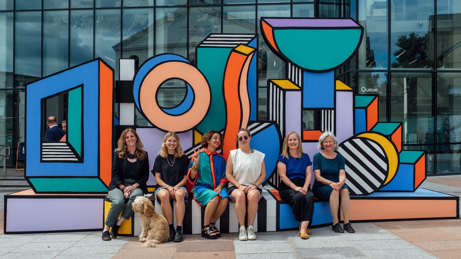 A group of people sat on a bright colourful work of art