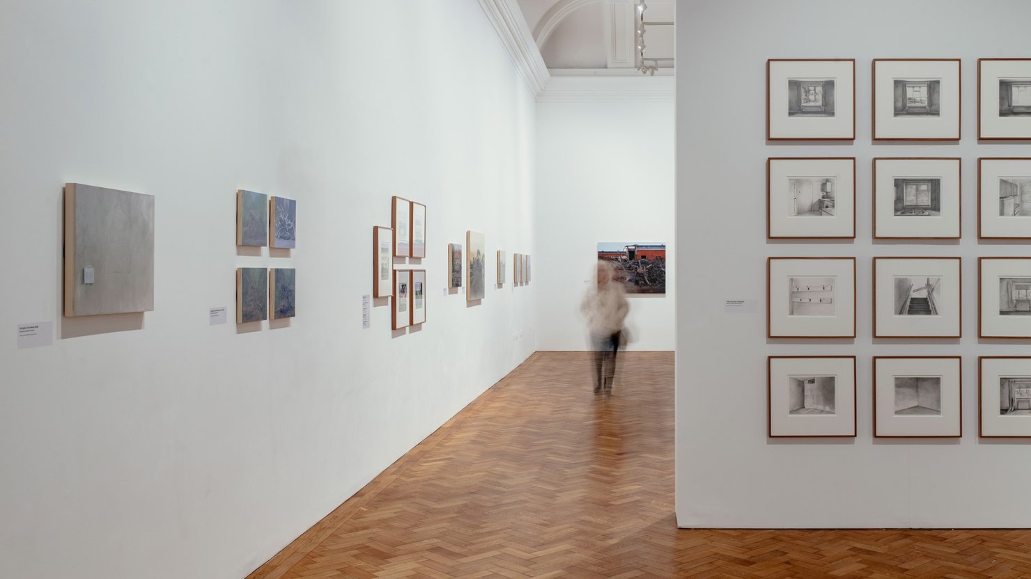 George Shaw paintings in gallery, some arranged in a grid with others on a side wall