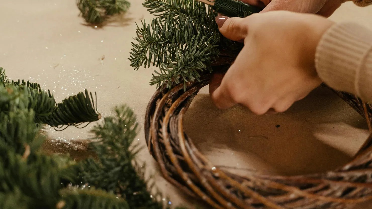 A person making a festive wreath with natural foliage