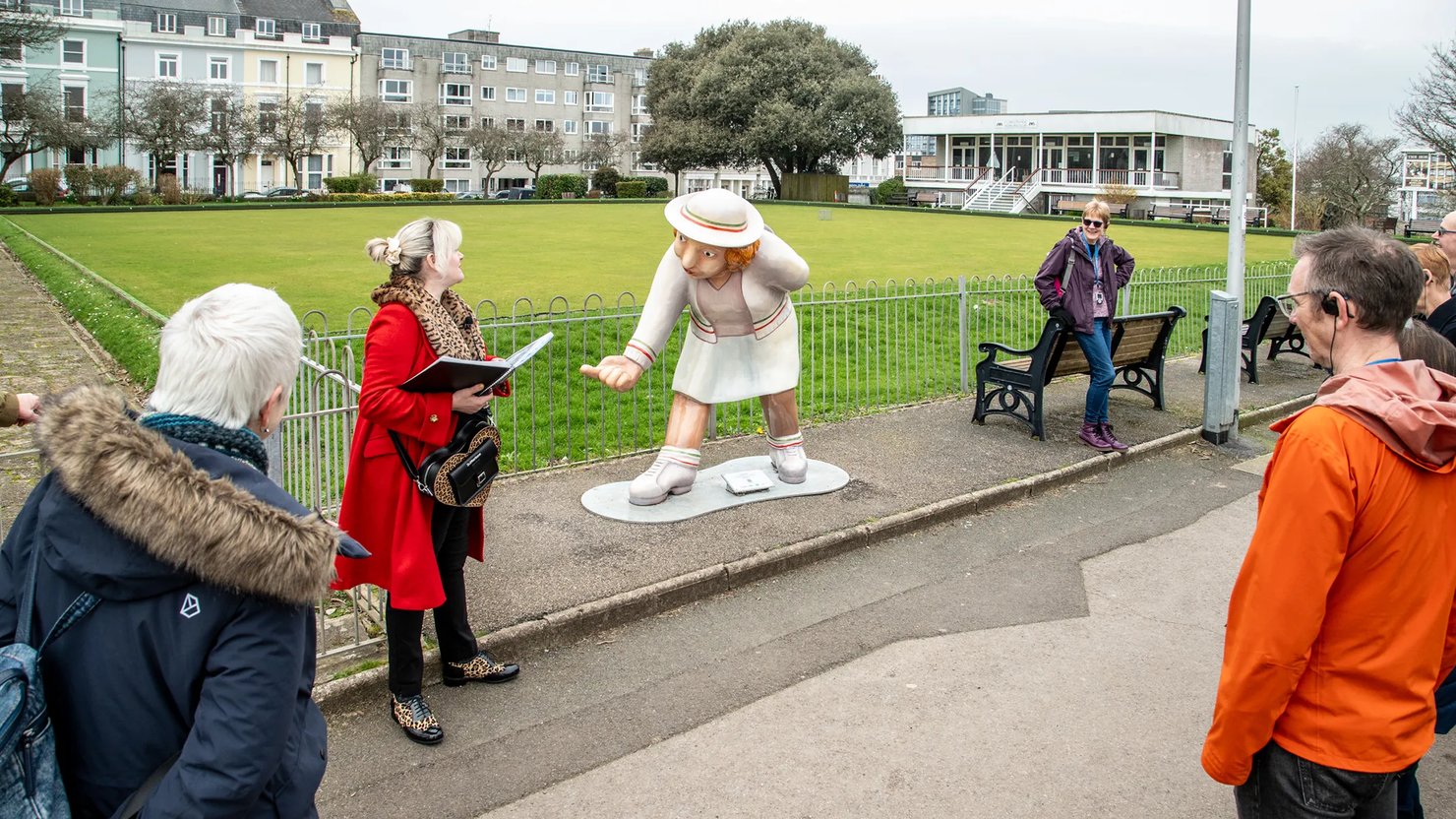 Photograph showing a group of people listening to a female talking about a sculpture of a lady bowling