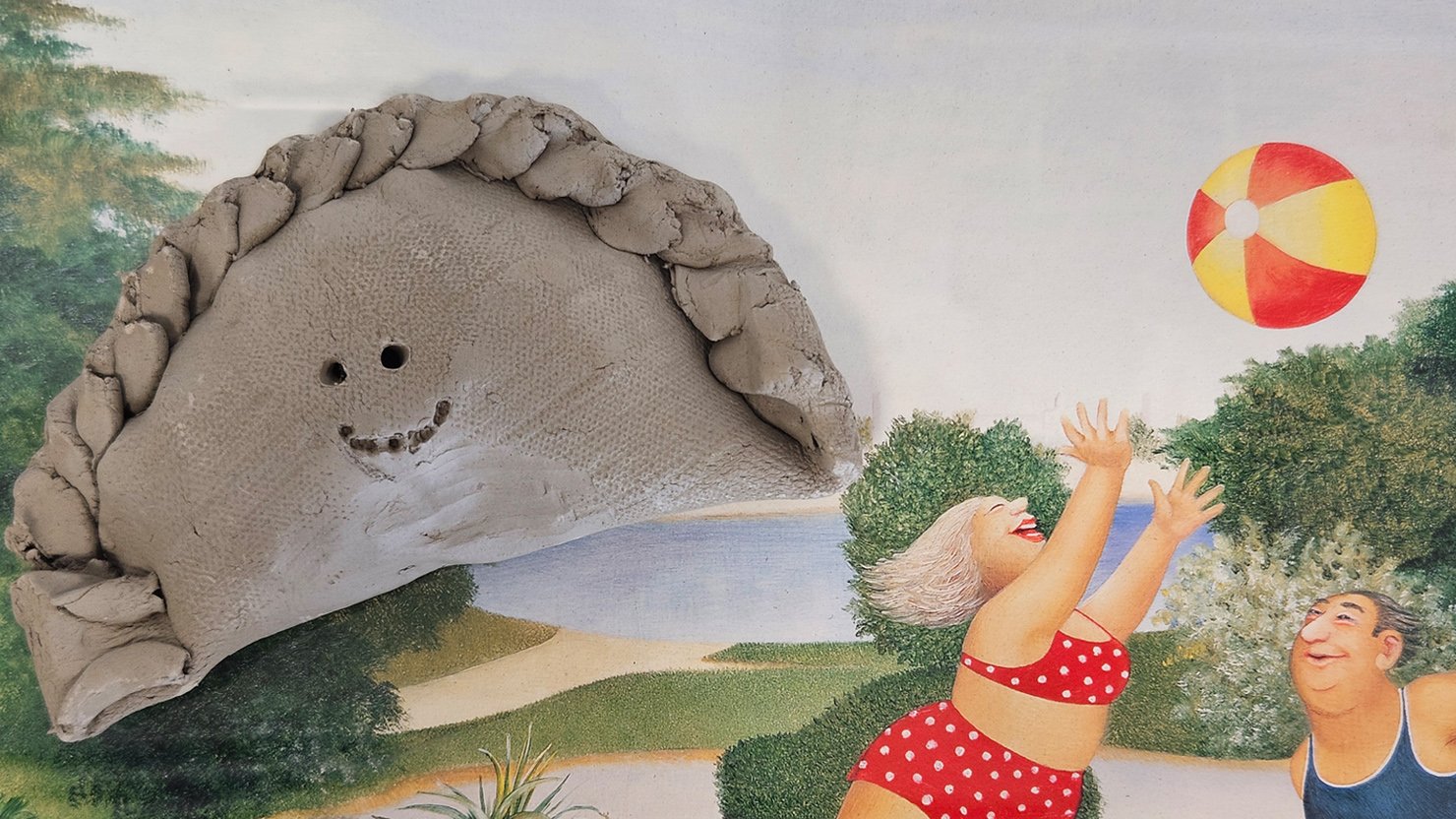 Photograph showing a clay pasty on top of a print showing a family having a picnic