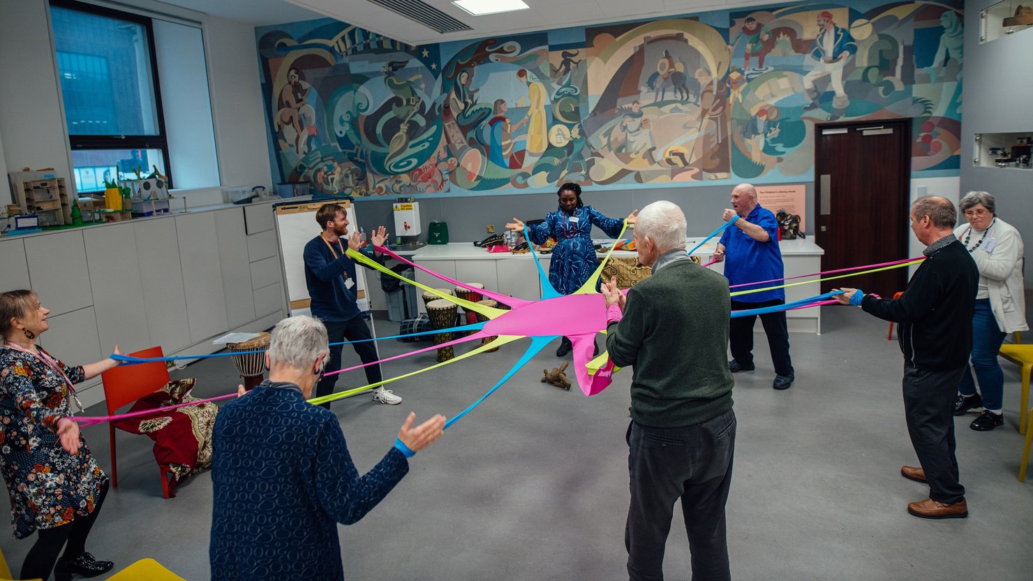 A group of people in a circle holding onto a stretchy piece of colourful fabric