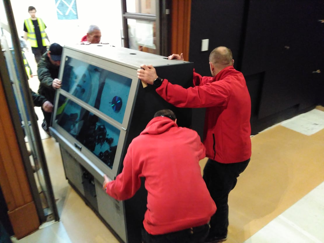 A group of people mainly dressed in red move a large piece of film equipment through a doorway