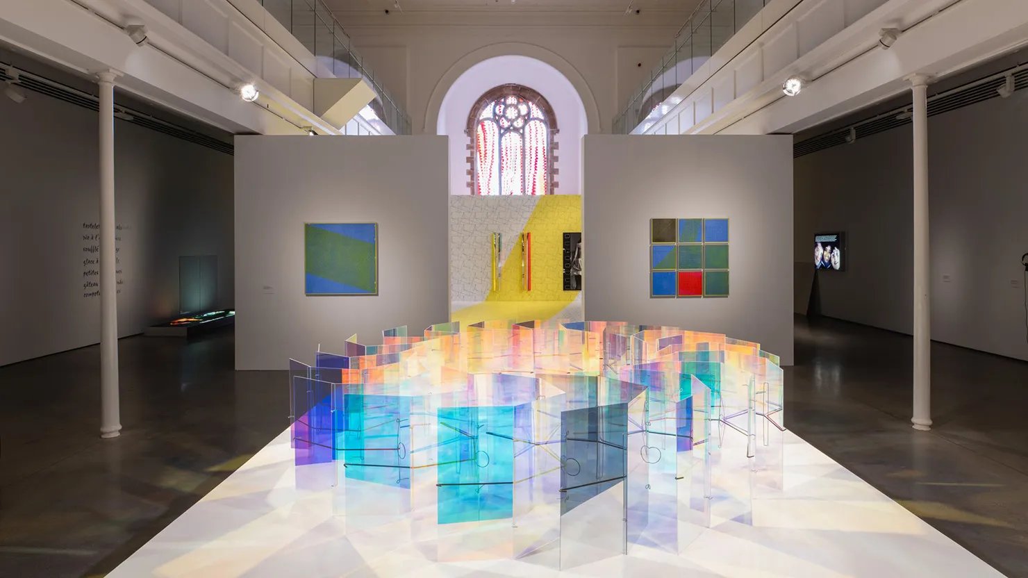 A photograph showing an exhibition in a gallery with colourful installations in the centre.