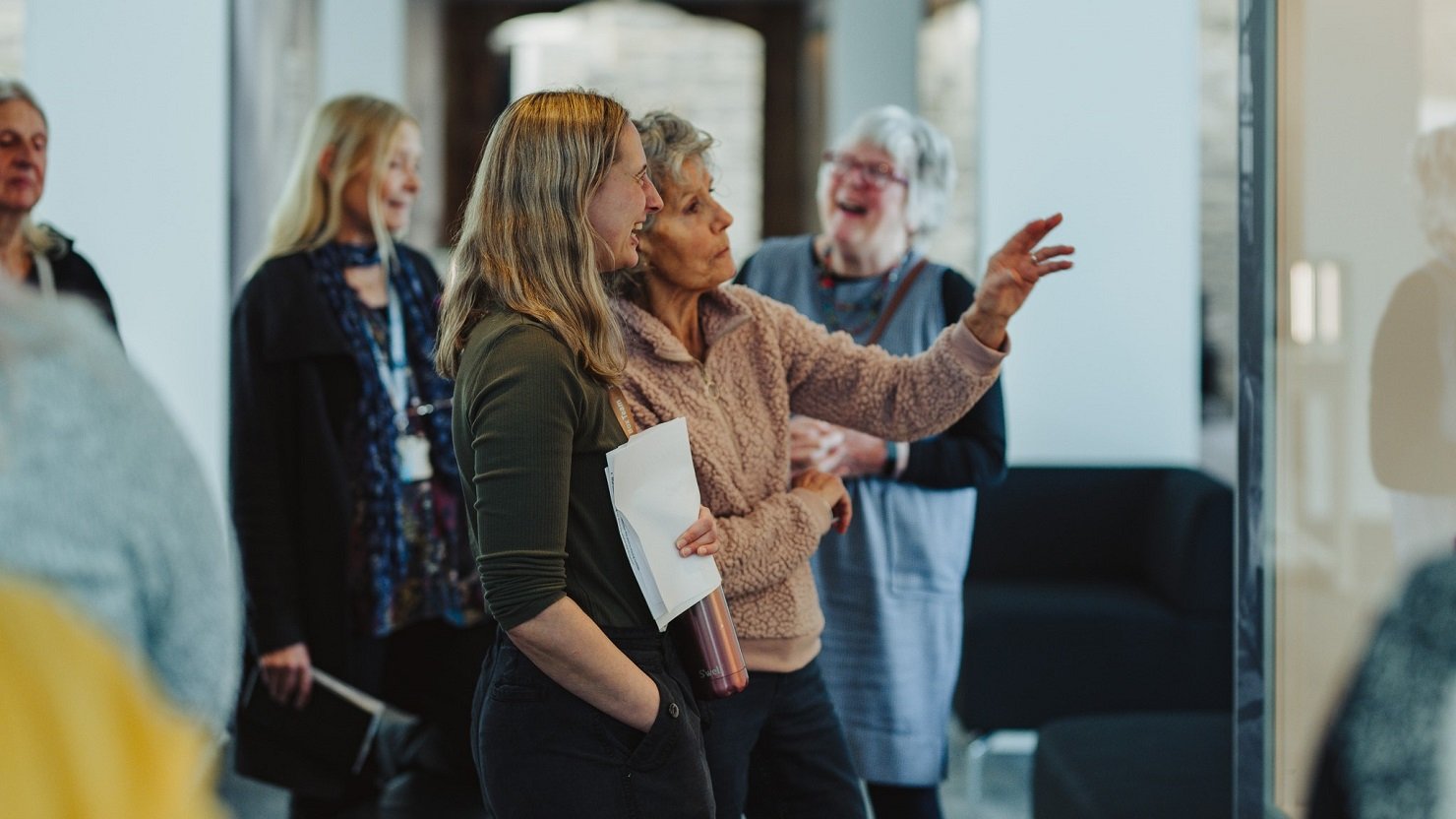 Two women stand taking while another woman laughs in the background