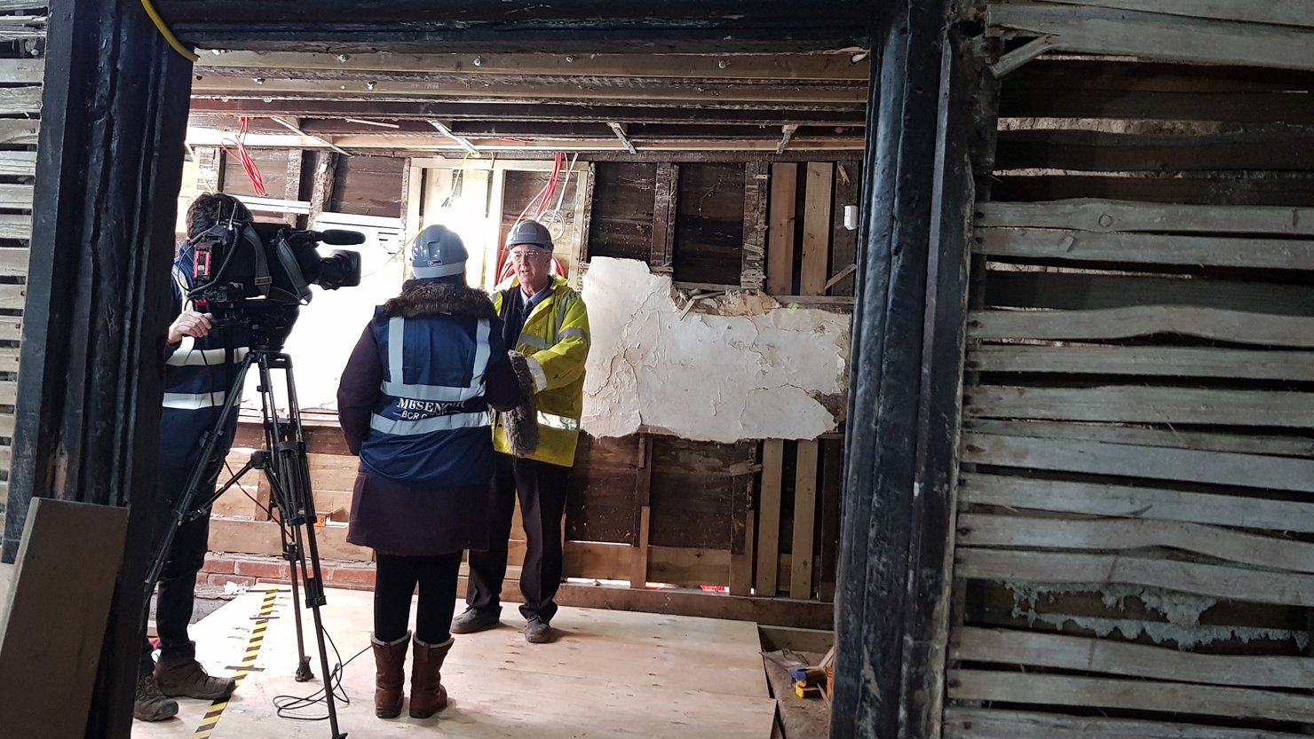 A man in a high vis vest talking to two people behind a film camera