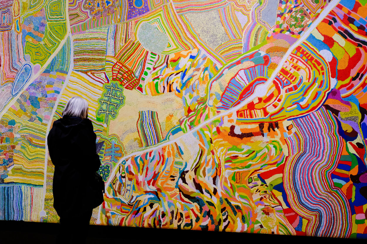 A female visitor looking at a large bright painting hanging on a wall