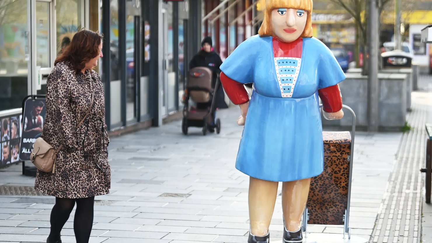 Photograph of a woman looking at a large sculpture of a woman with a shopping trolley