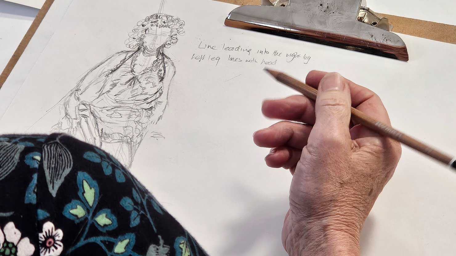 A woman's hand holding a pencil as she draws a female figure