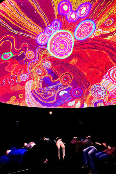 Visitors watching a projection of an animated artwork inside the 'Songlines' immersive dome