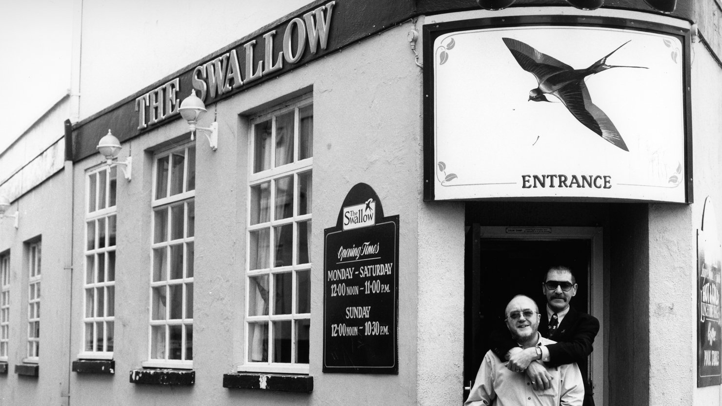 Black and white image of two men standing together in the entrance of The Swallow pub in Plymouth