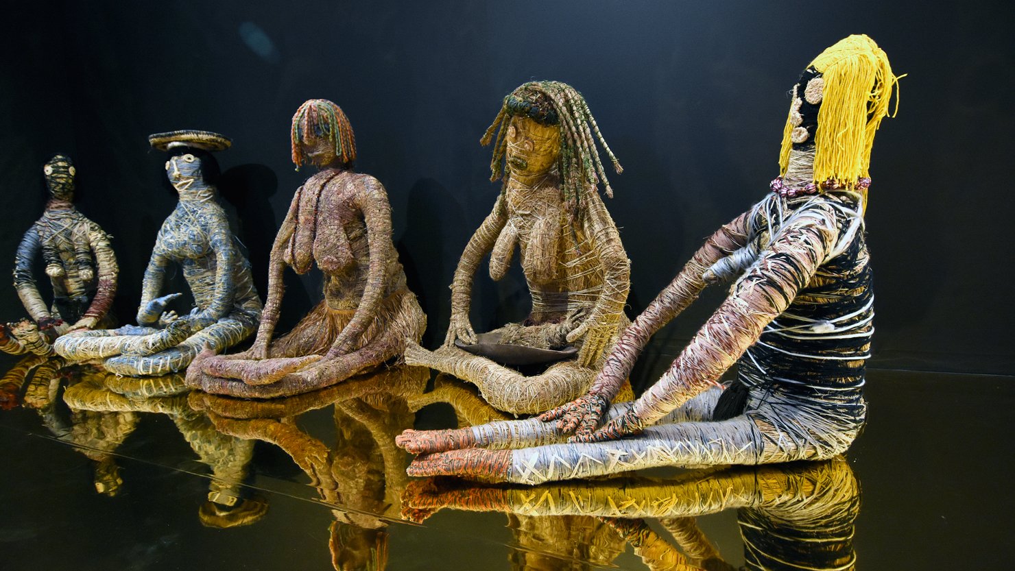 A group of woven female figures on a gold plinth