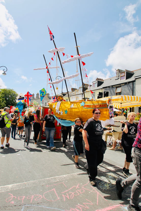 A group of people taking part in a community parade and carrying a boat made from card