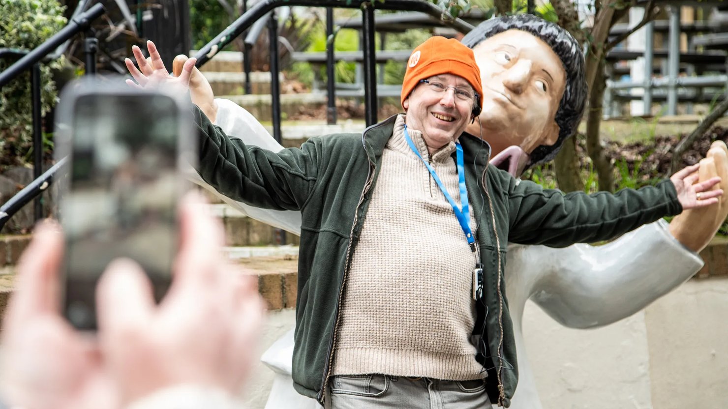 Photograph showing a man posing in front of a statue of a man with arms outstretched
