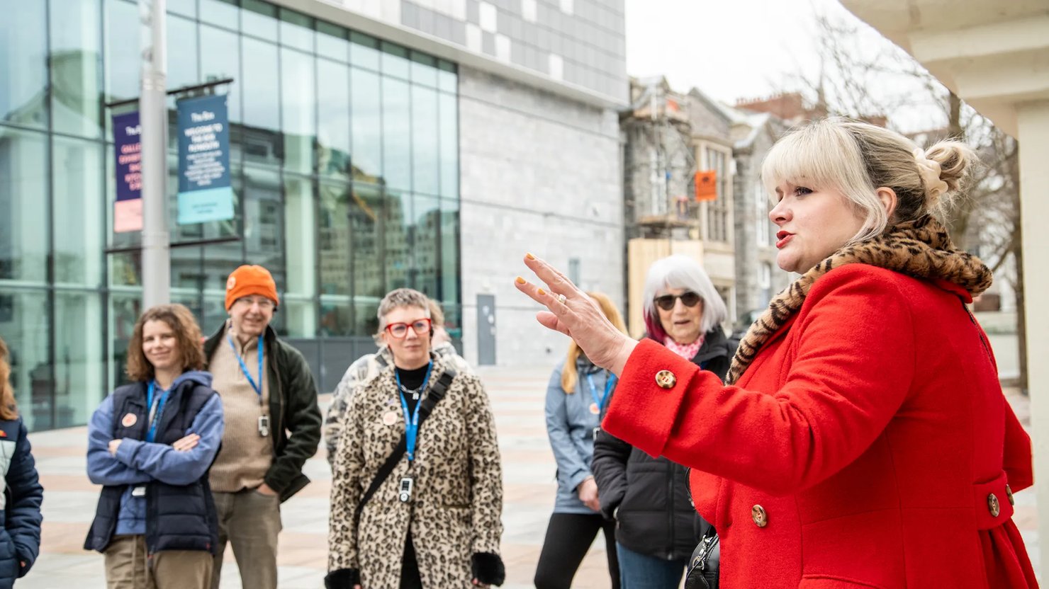Photograph of a group listening to a female comedian dressed in a red coat