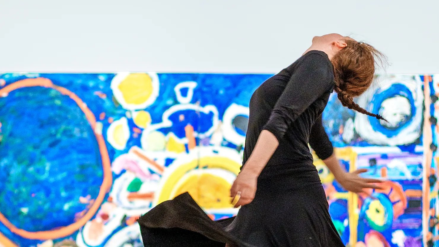 Photograph showing a dancer rehearsing a performance in front of a large abstract painting in a gallery