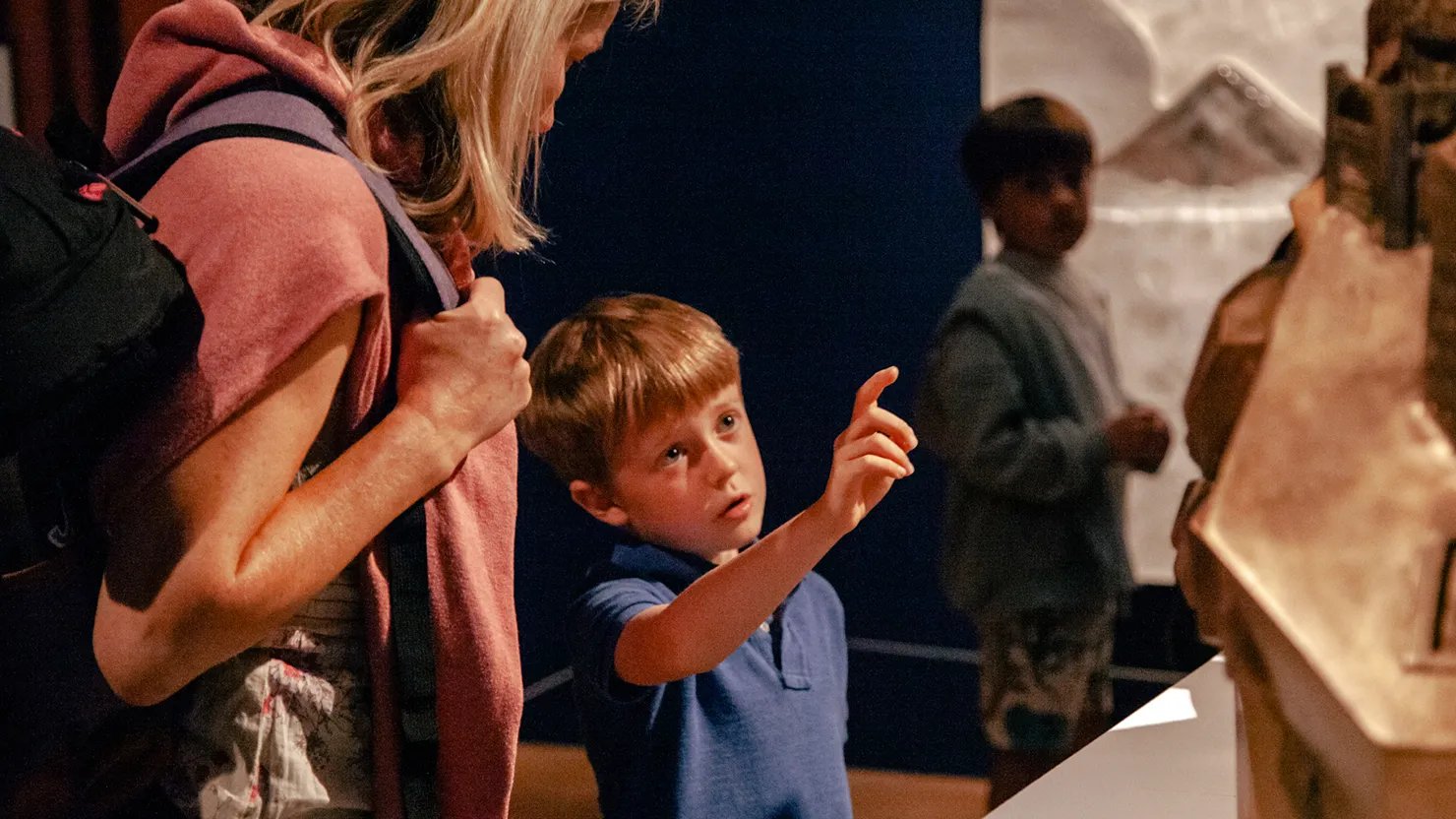 Photograph of a child and parent. The child is pointing and looking at a museum display.