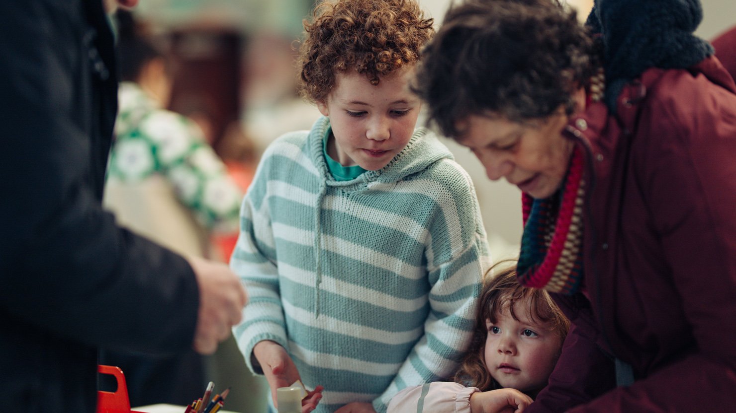 A boy standing with his family at a table during a workshop at The Box Plymouth