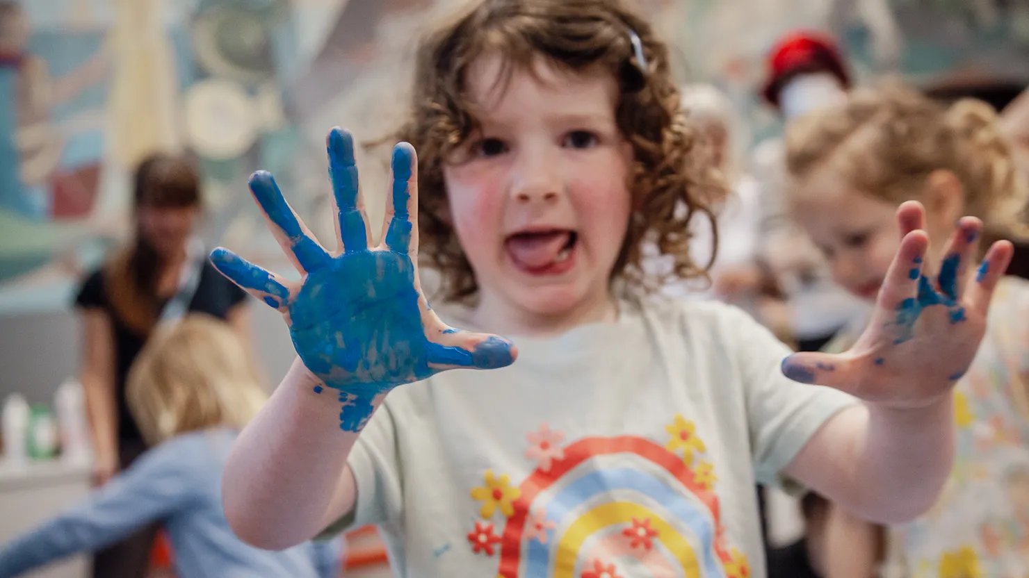 A young girl showing paint covered hands in a preschooler workshop