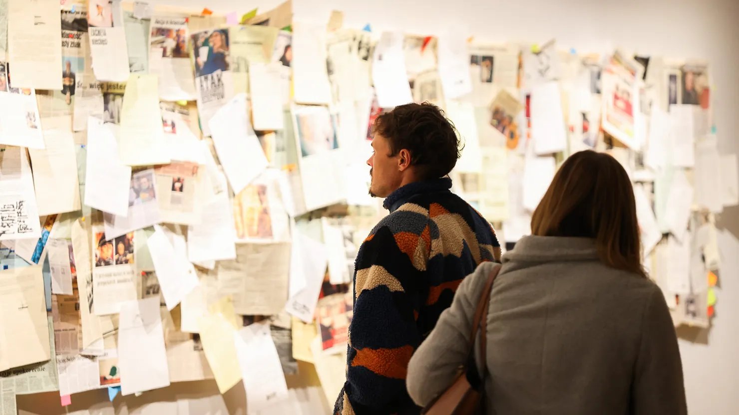 Visitors looking at artwork made of paper documents on a wall
