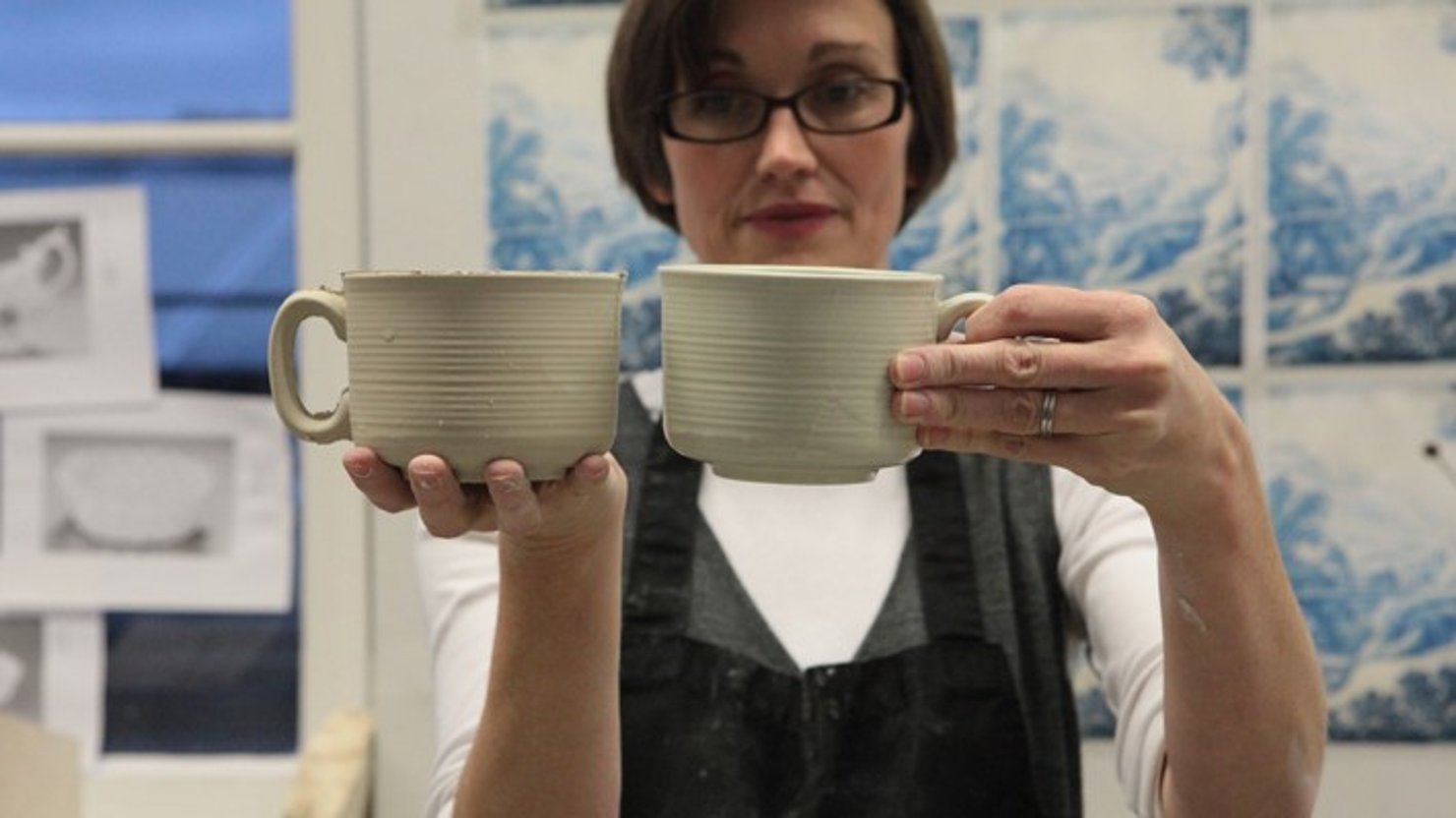 Artist Clare Twomey holds up two ceramic mugs in her studio at the V&A, London