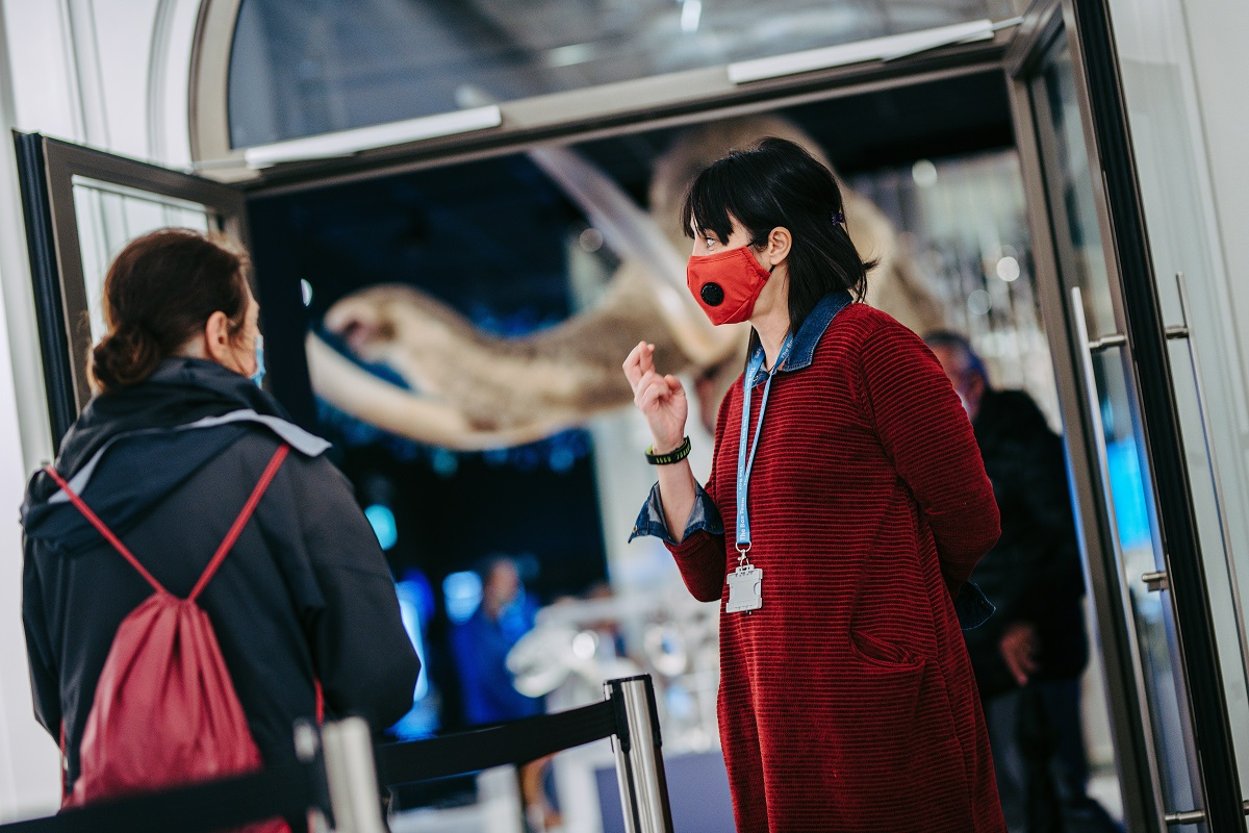 An image of two people in face masks at The Box, Plymouth with the mammoth in the background