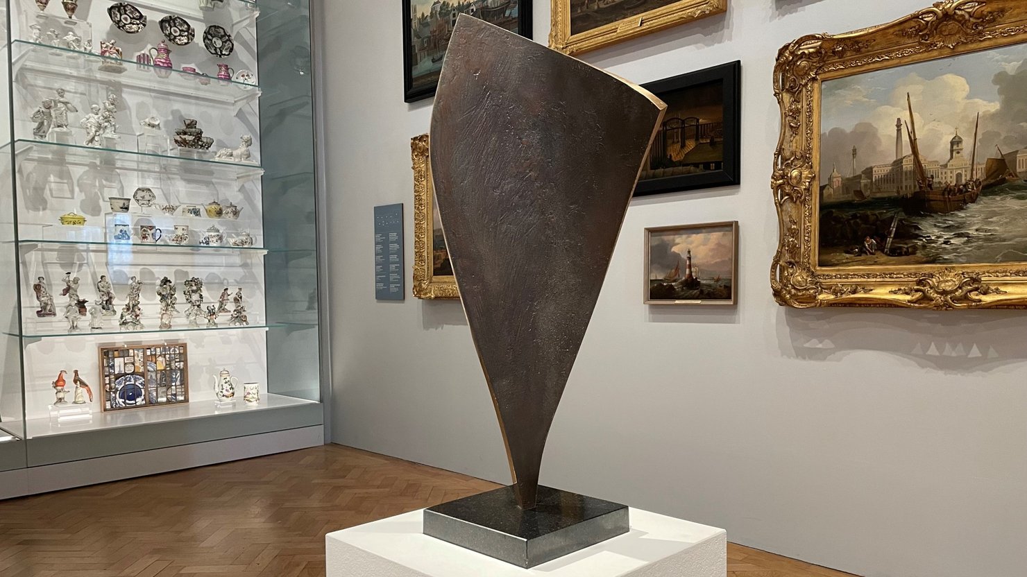 Photograph of a bronze sculpture in a sail shape in an art gallery.