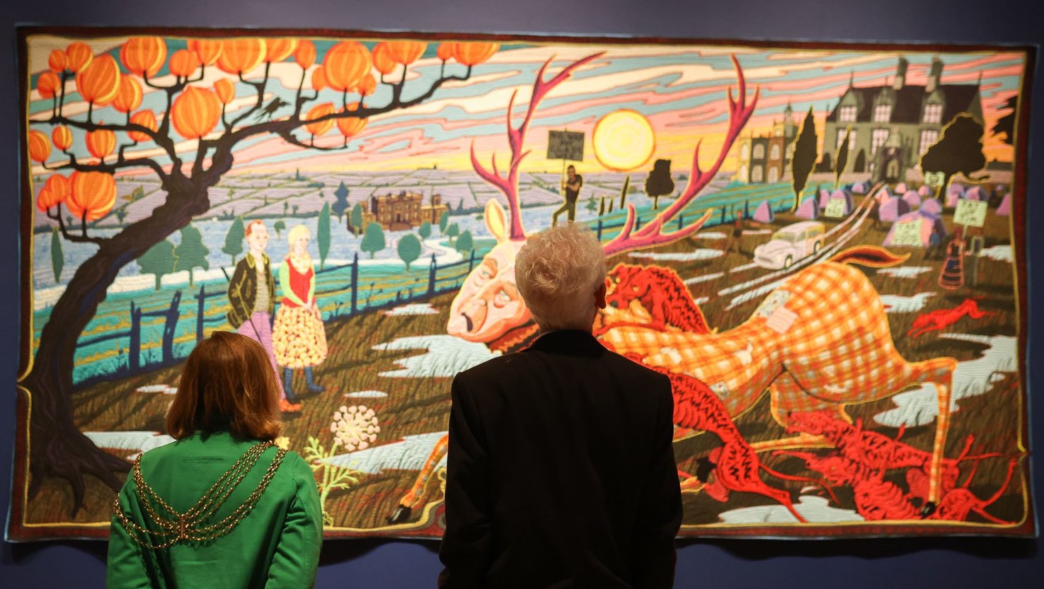 Visitors looking at a large colourful tapestry by artist Grayson Perry