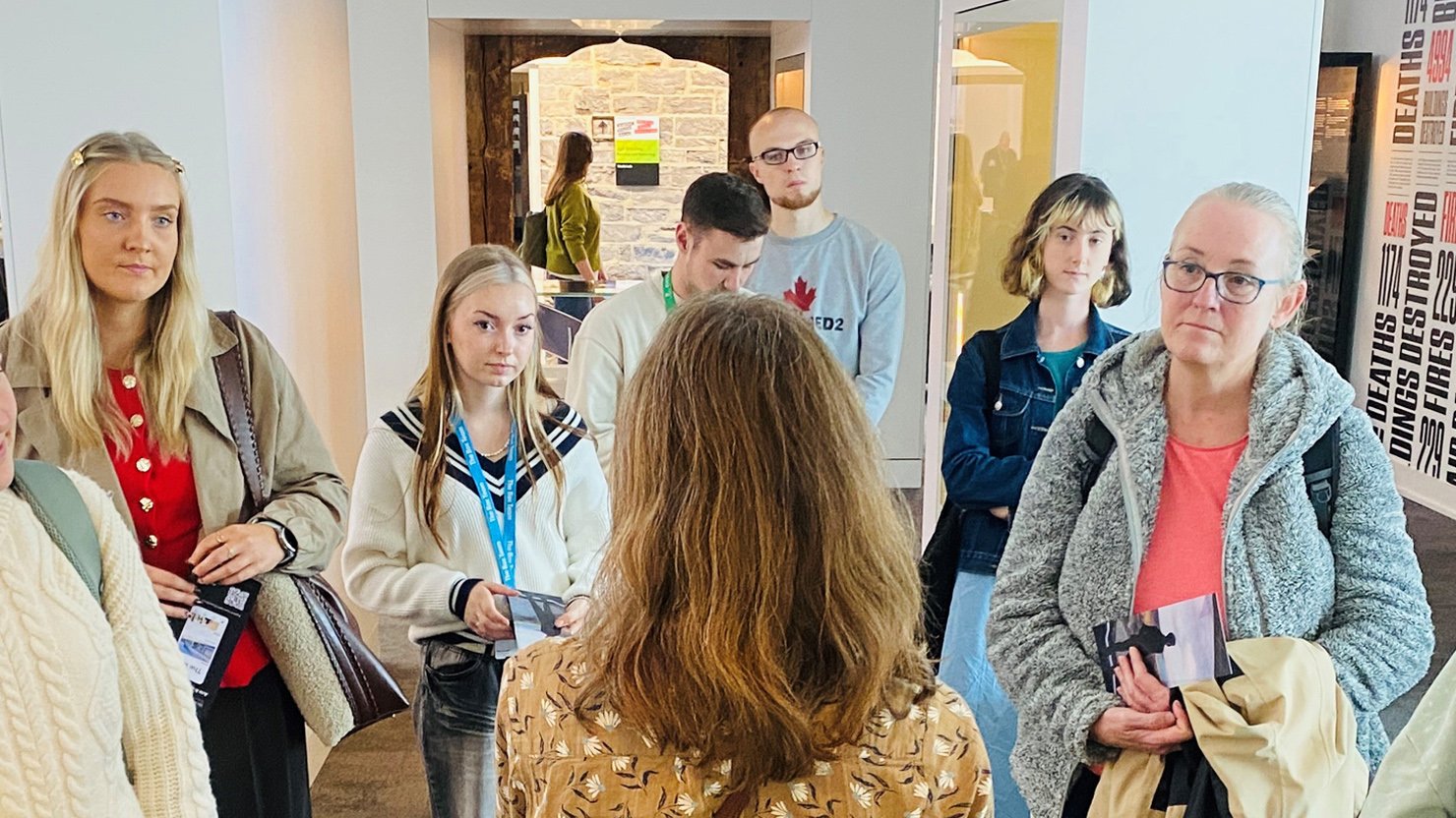 A group of people standing in a gallery listening to a speaker