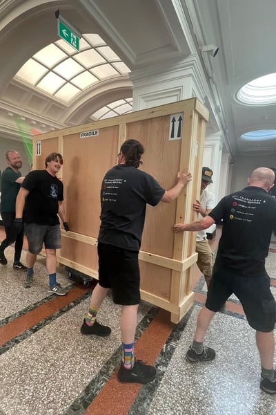 A group of people moving a heavy painting in a large wooden palette