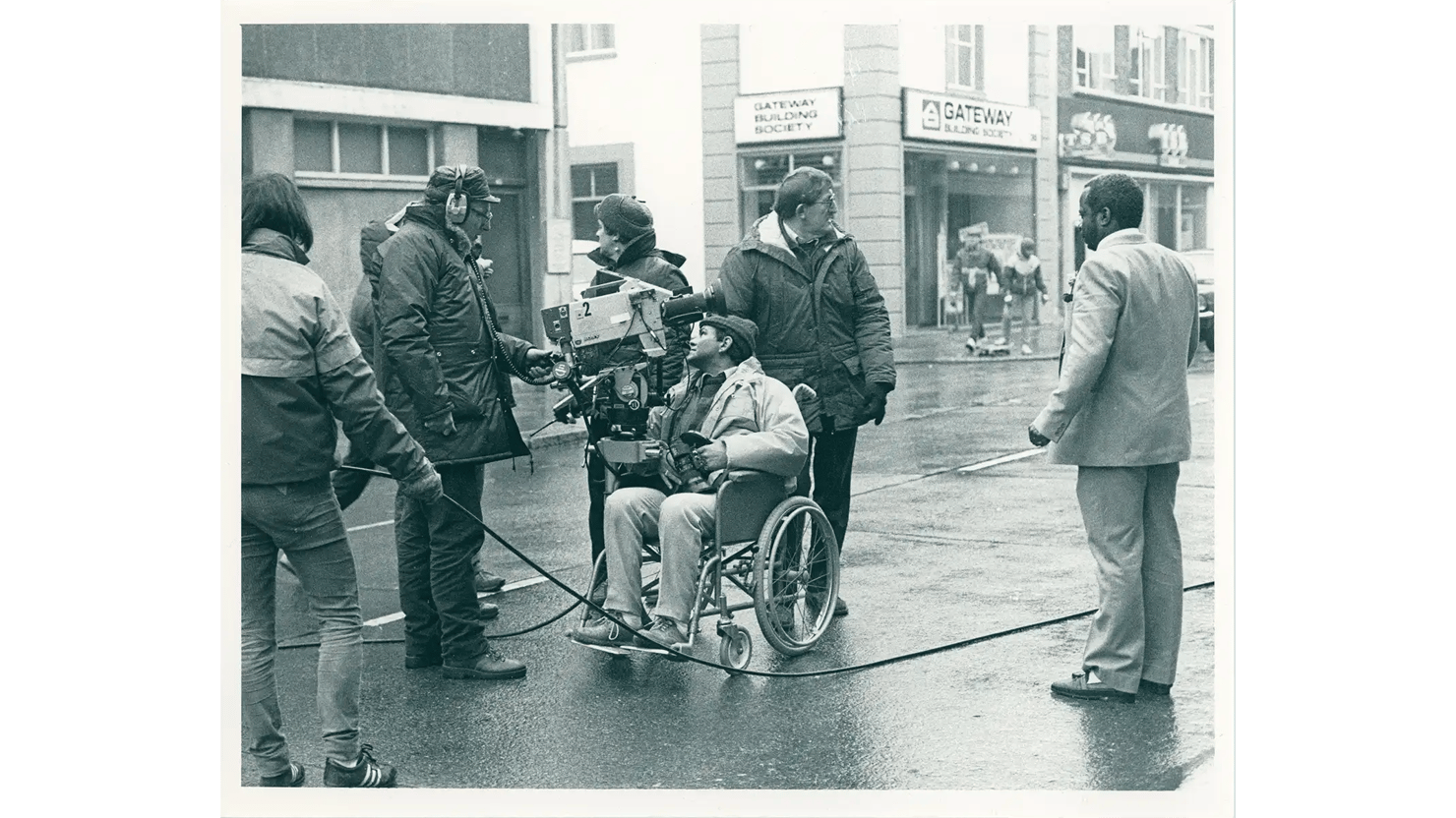 Photograph showing a group of actors and tv crew filming on location in a street