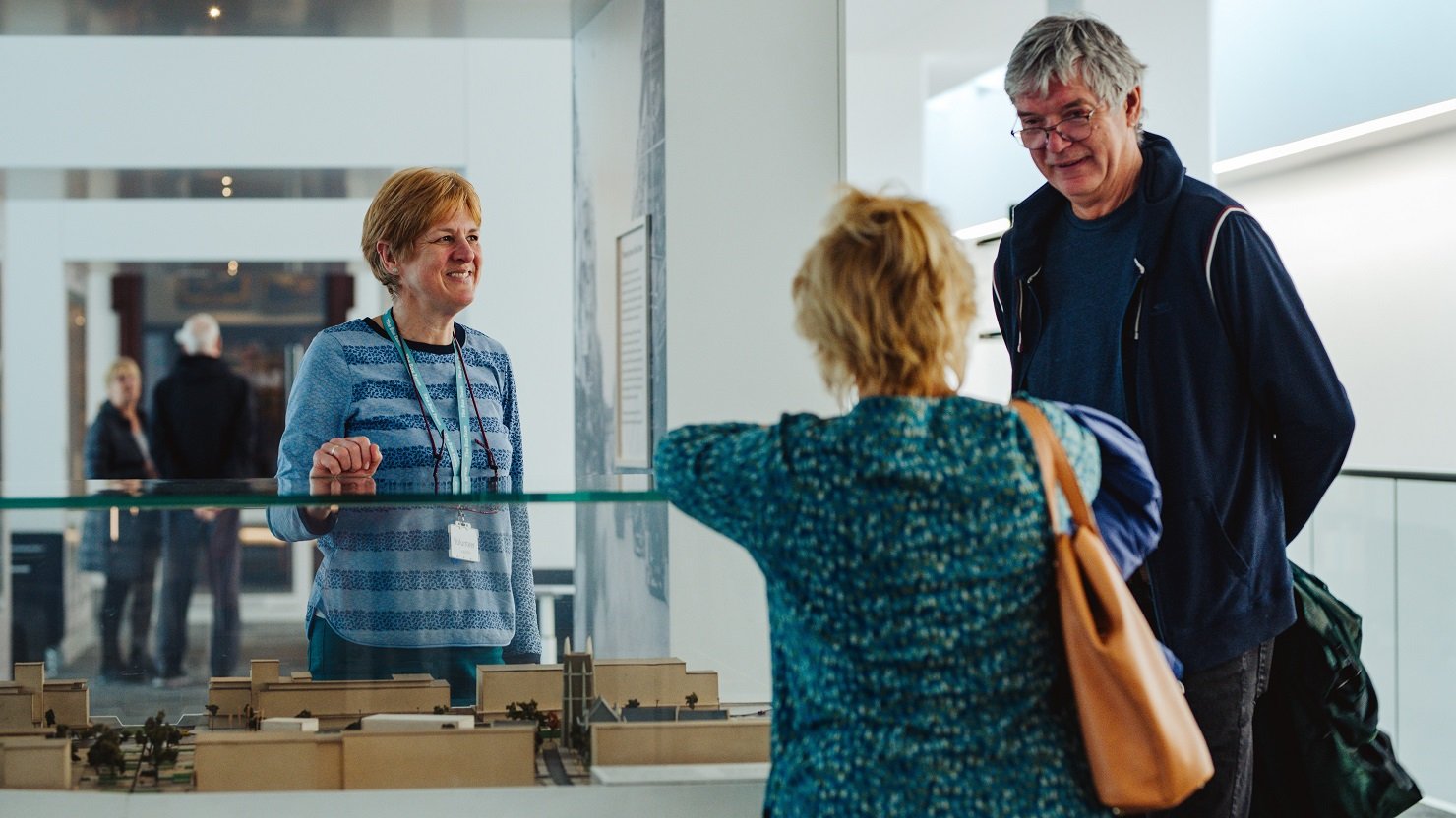 A female volunteer in an art gallery talking to two visitors