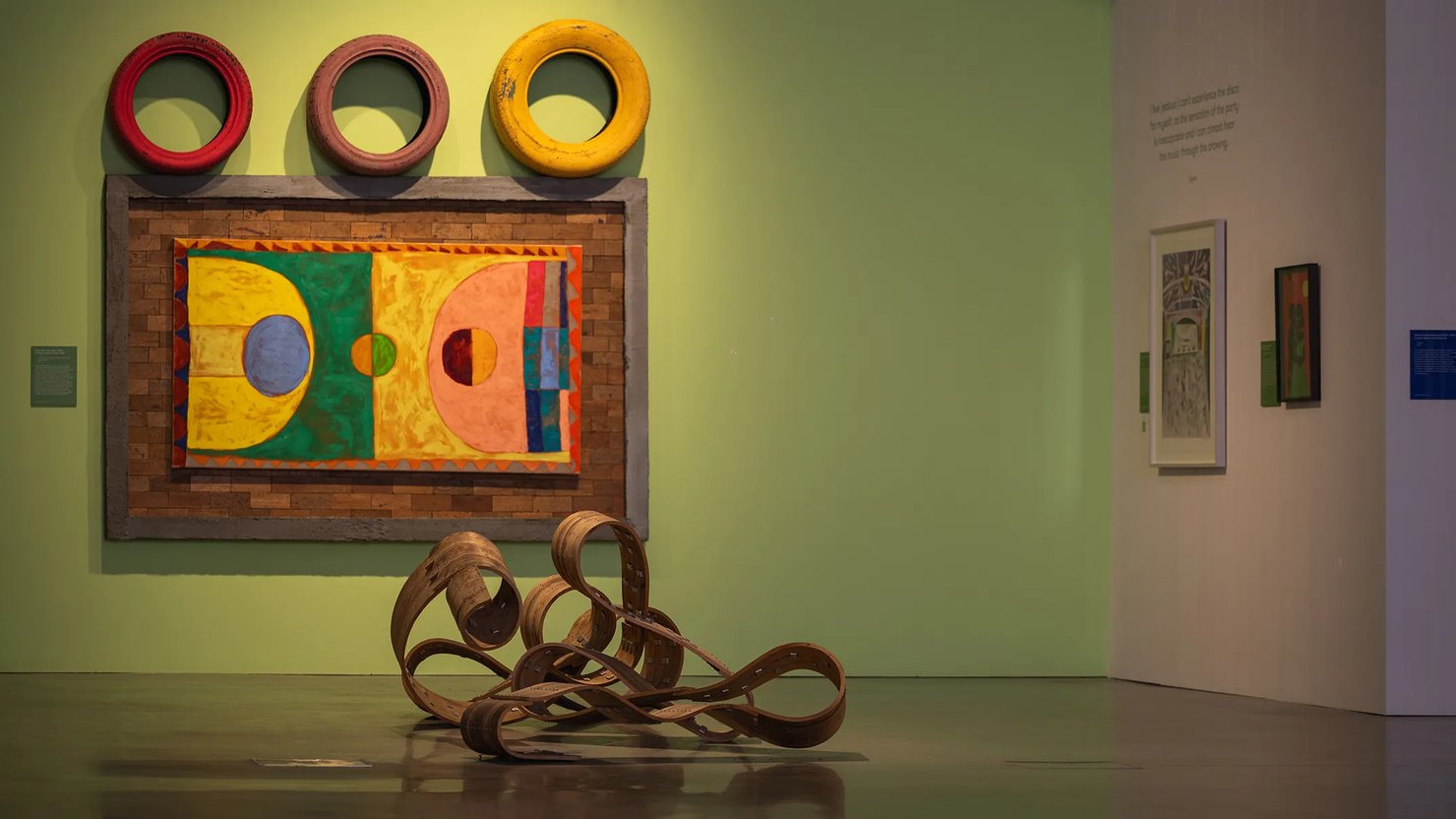 Photograph showing 2D works on a wall with a sculpture in front