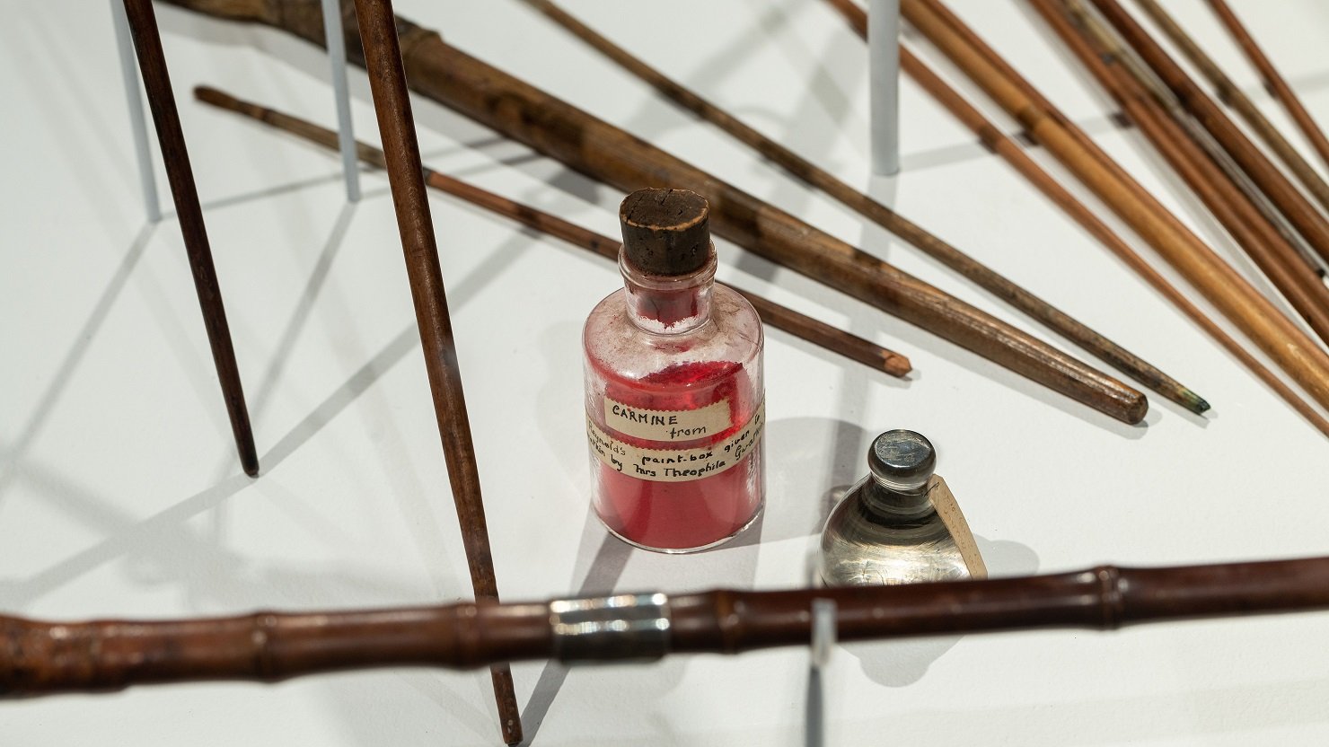 A bottle of red carmine pigment and artist brushes in a case