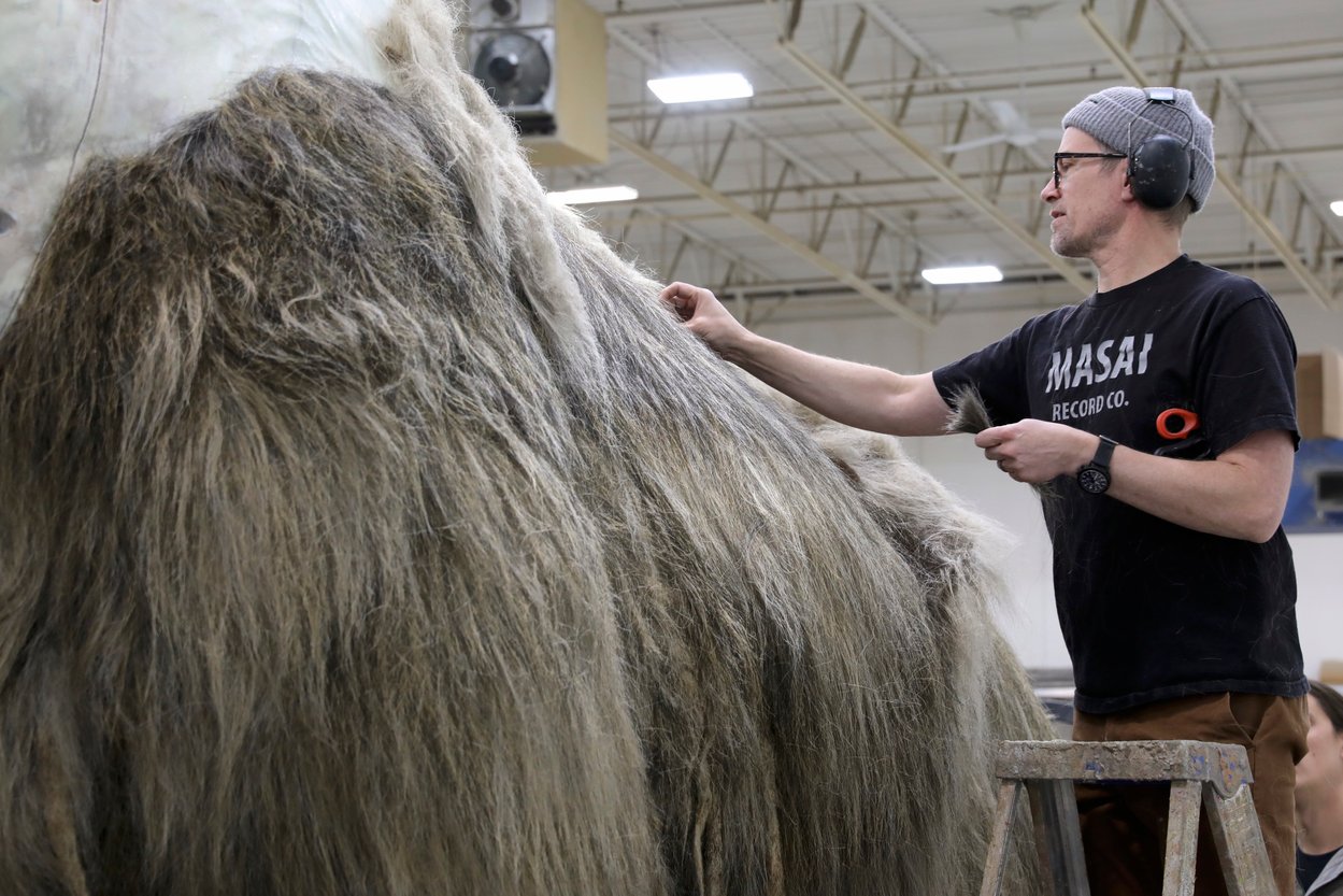 A man adding fur to a large-scale replica of a woolly mammoth