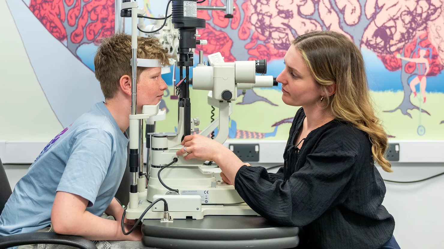 A woman operating an optometry machine whilst a boy looks into it