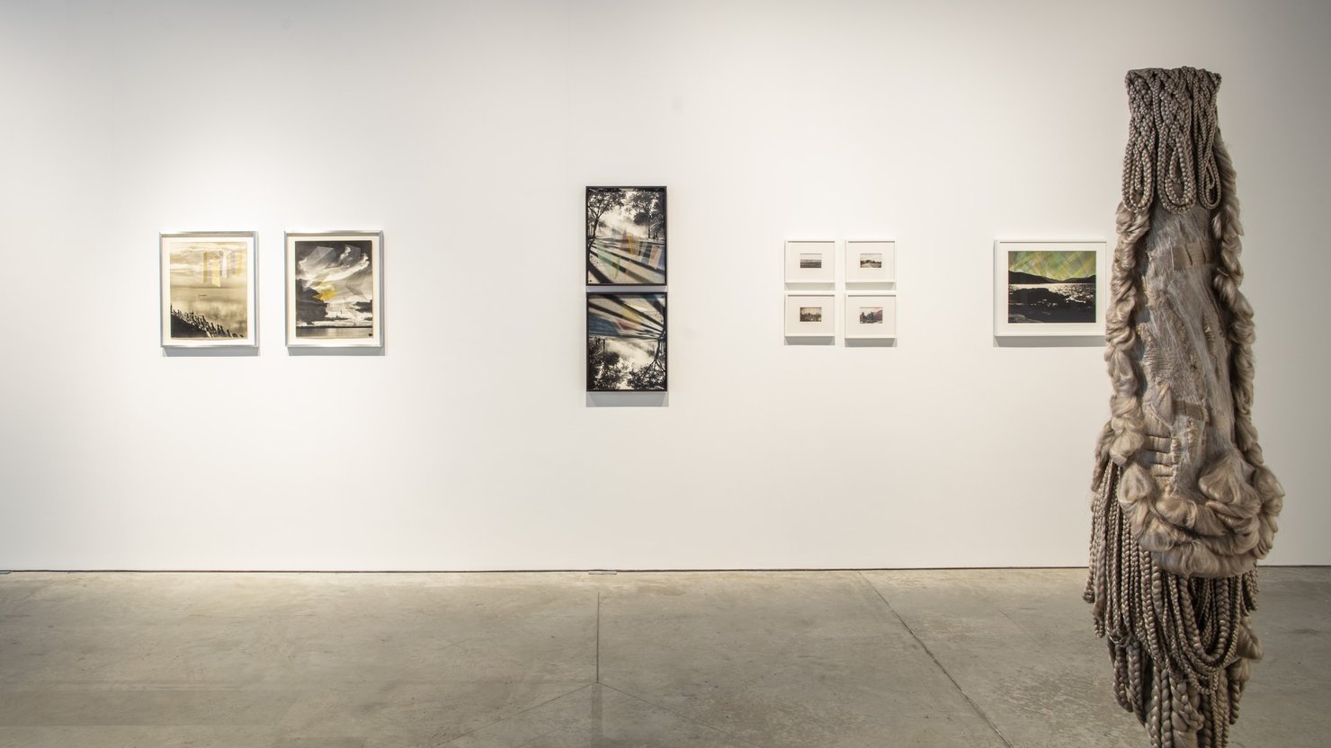 Artworks hanging on a gallery wall, with a sculpture made of hair seen in the right of the image