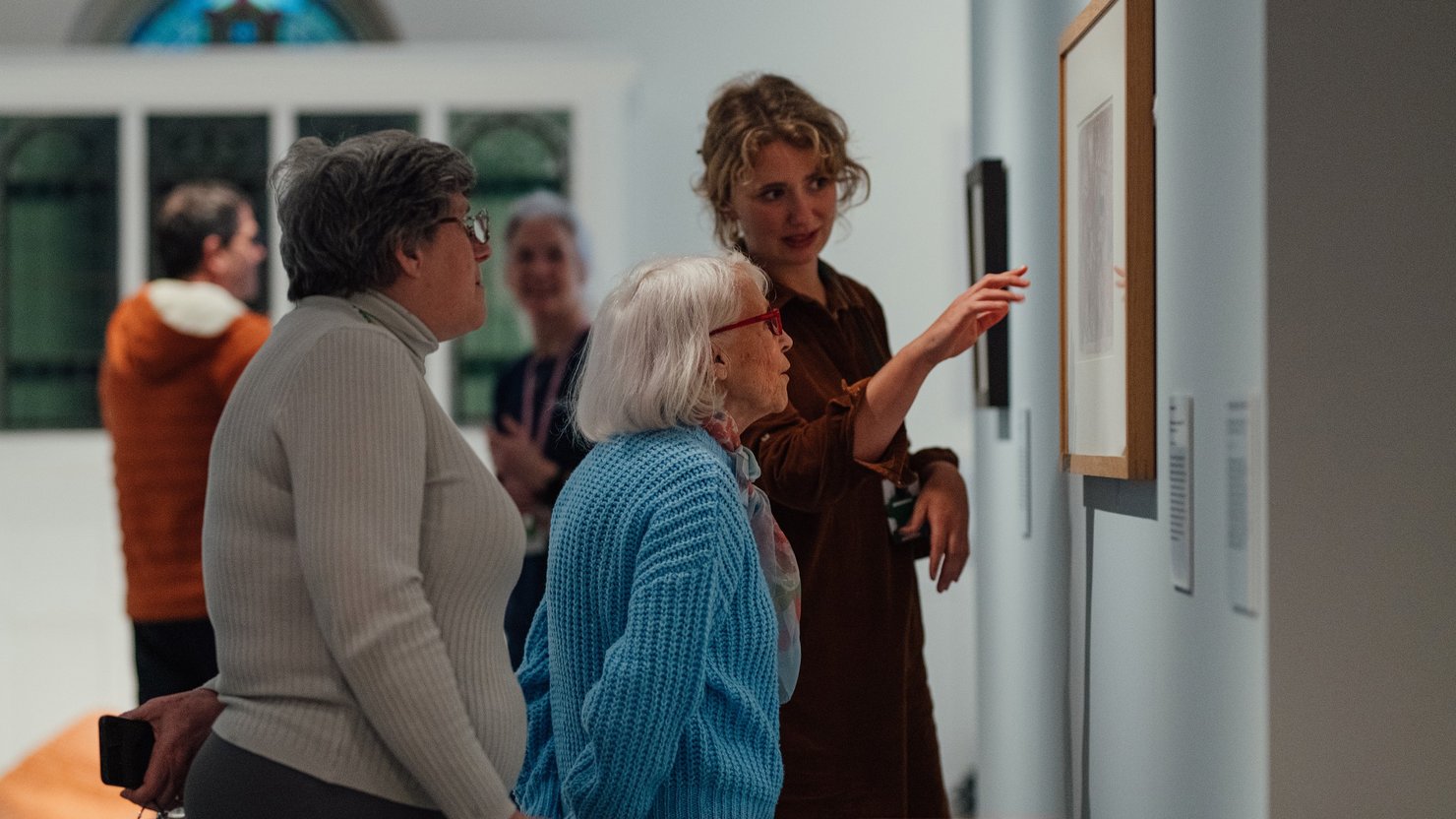A photograph showing a group of workshop attendees talking about an artwork with a member of staff