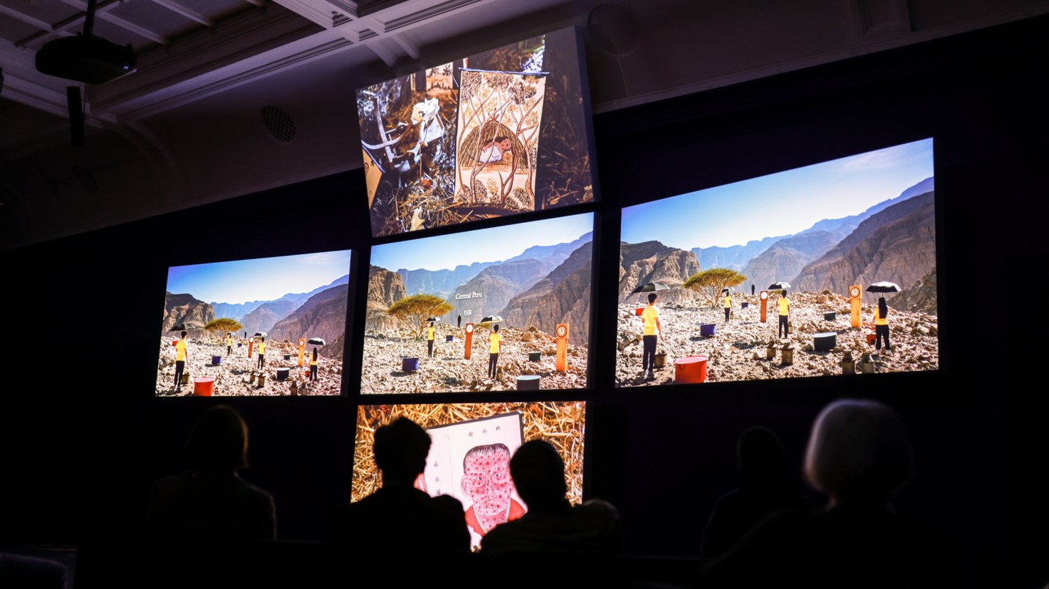 Audience watching film installation with screens showing mountainous landscapes
