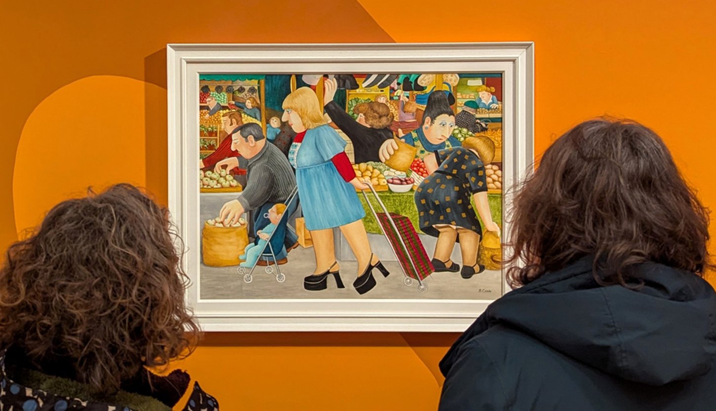 Photograph showing two women looking at a painting of a woman shopping in a market