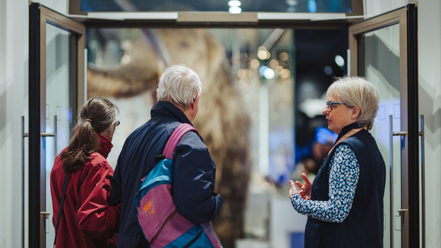 A female volunteer in an art gallery talking to two visitors