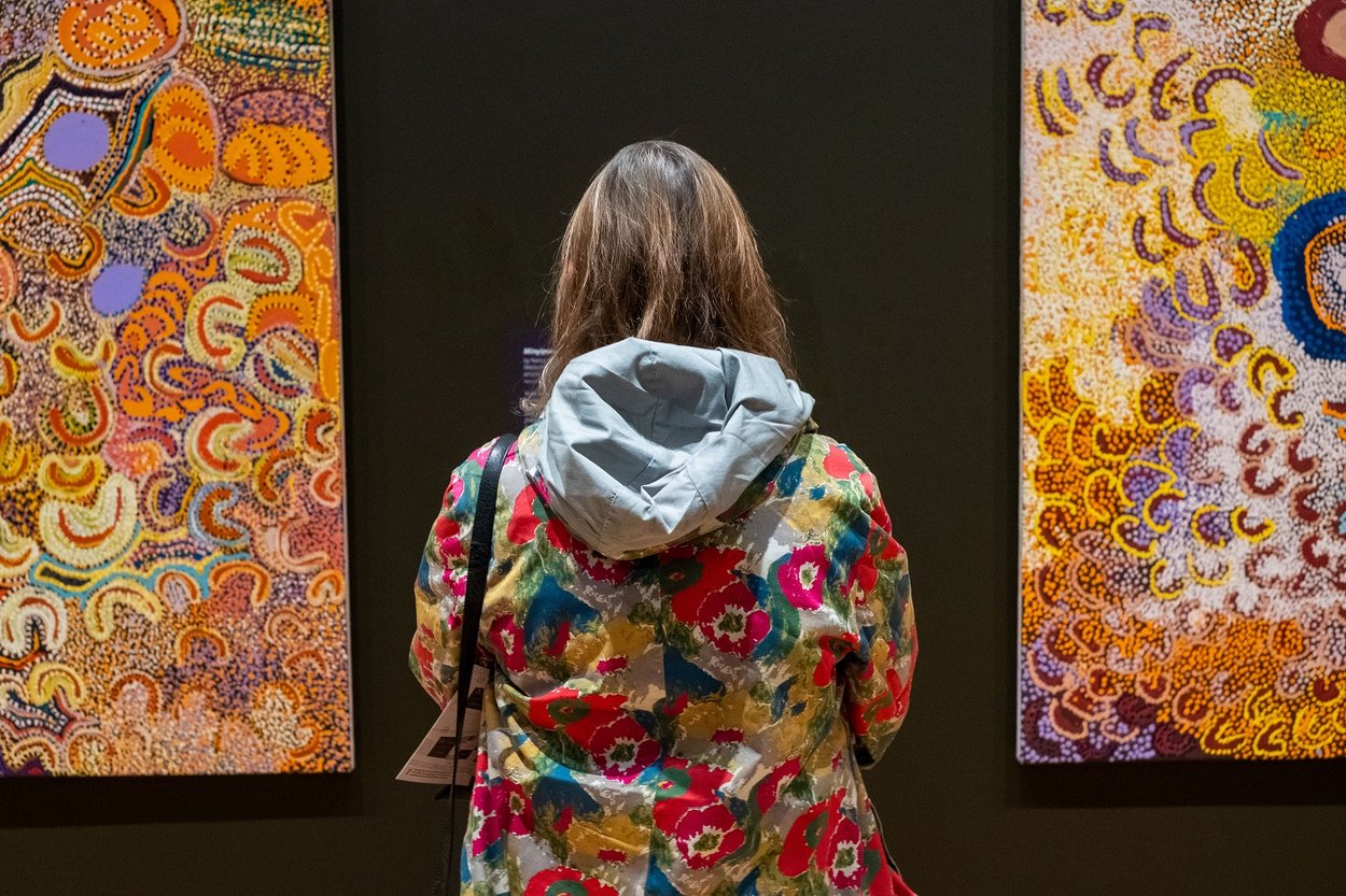 A woman stands between two paintings hanging on a wall. Image © Getty.