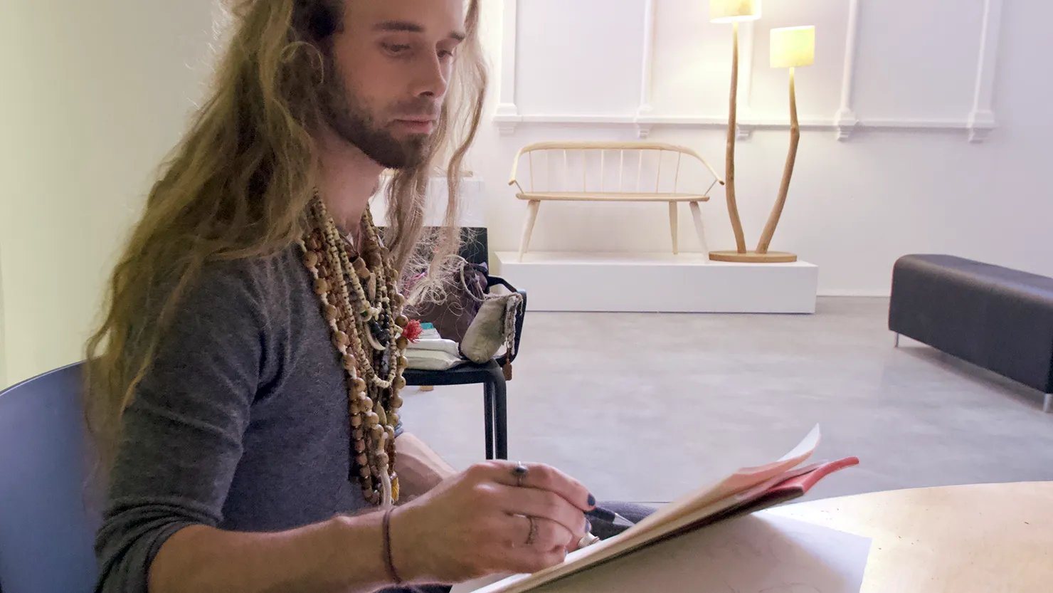 Photograph showing a male sketching whilst sitting in a gallery space.